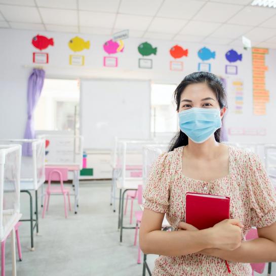 Female educator standing in empty classroom wearing mask